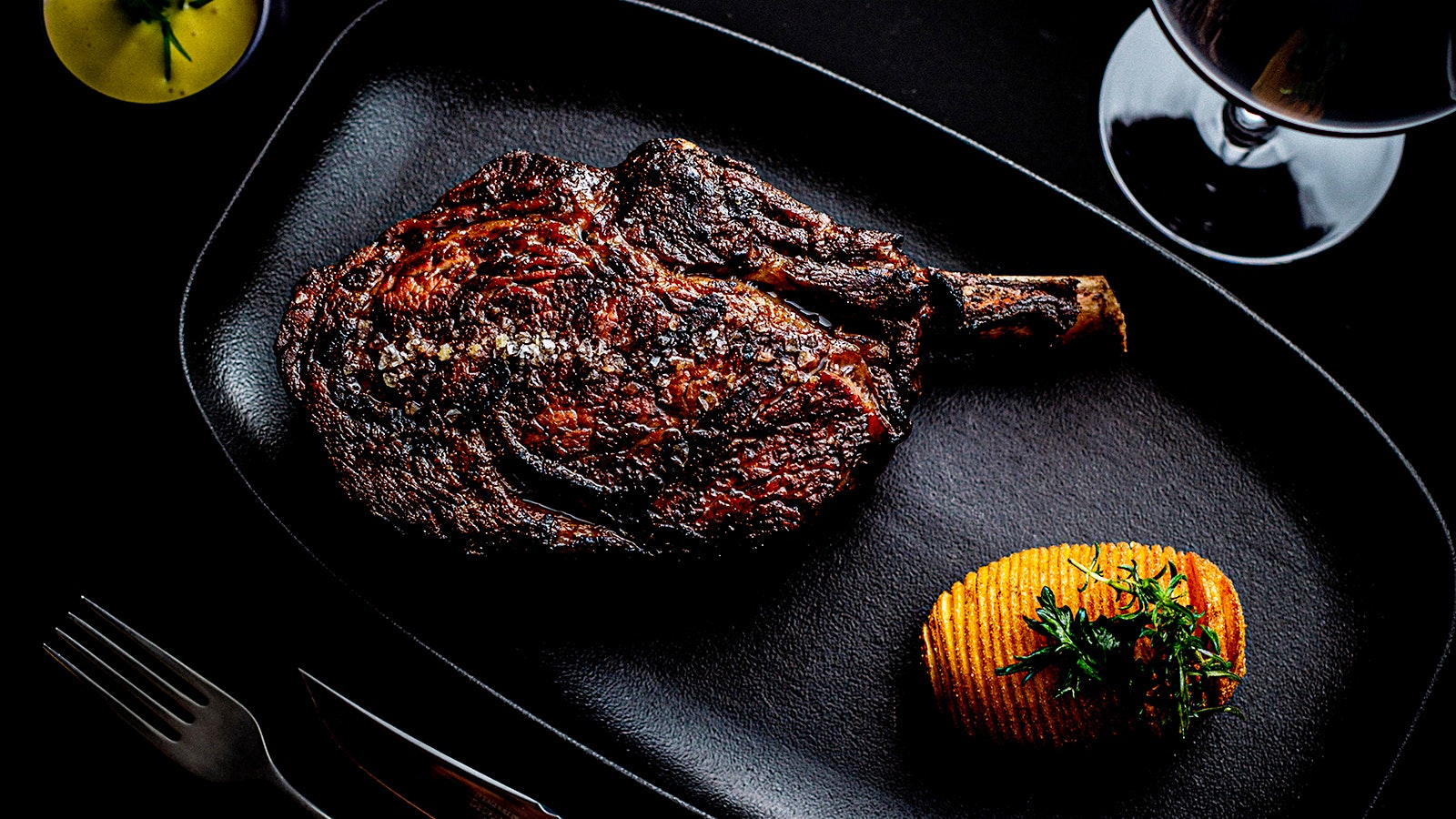 Steak and a hasselback potato next to a glass of red wine